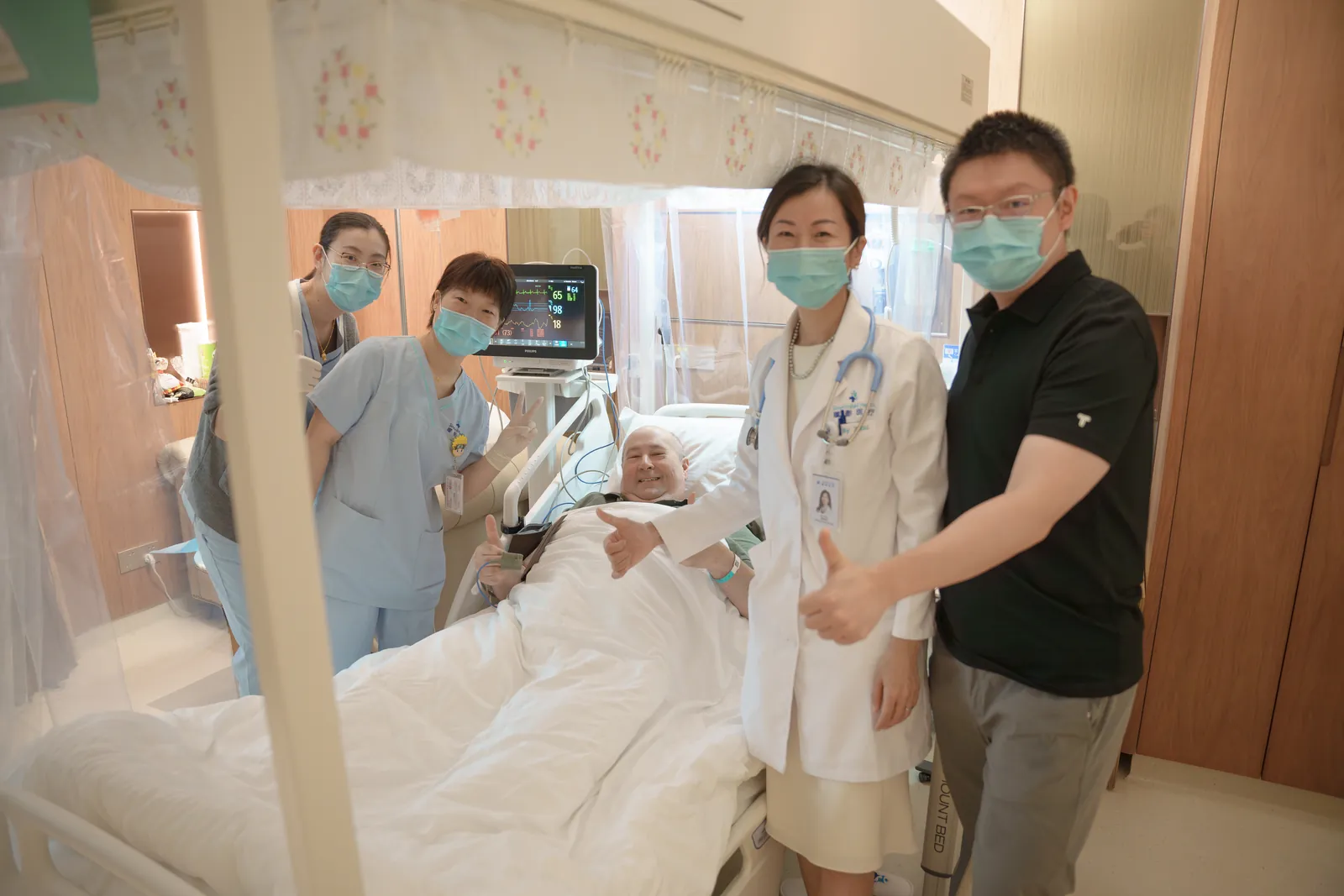 A CAR T-cell therapy patient giving a thumbs-up from his bed alongside his SinoUnited Health care team in Shanghai.