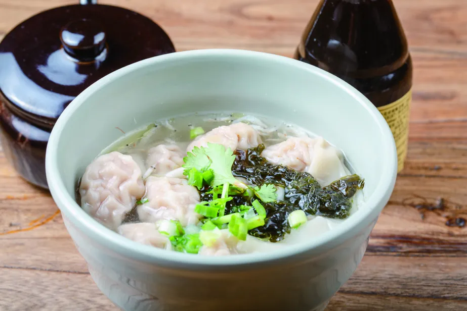 A bowl of wonton soup with greens and spring onion